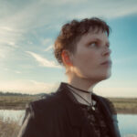 Close-up of Tennell looking up toward sky with clouds behind her.